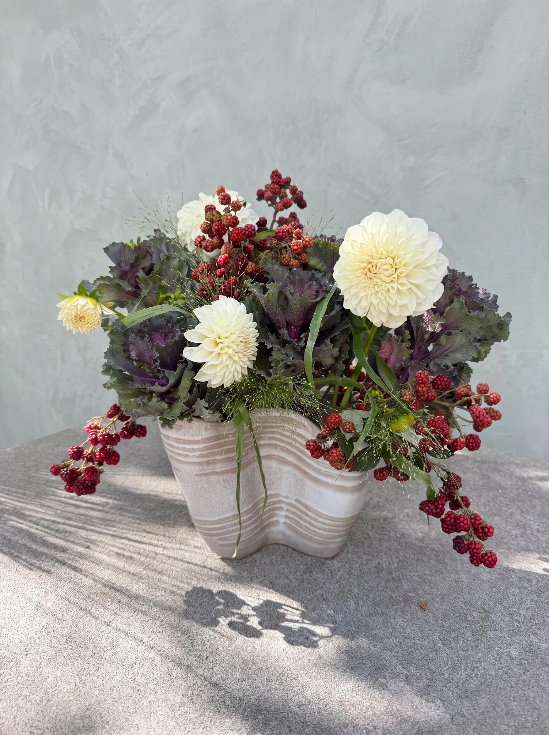 White dahlias, purple kale and red berries in a sculptural striped vase