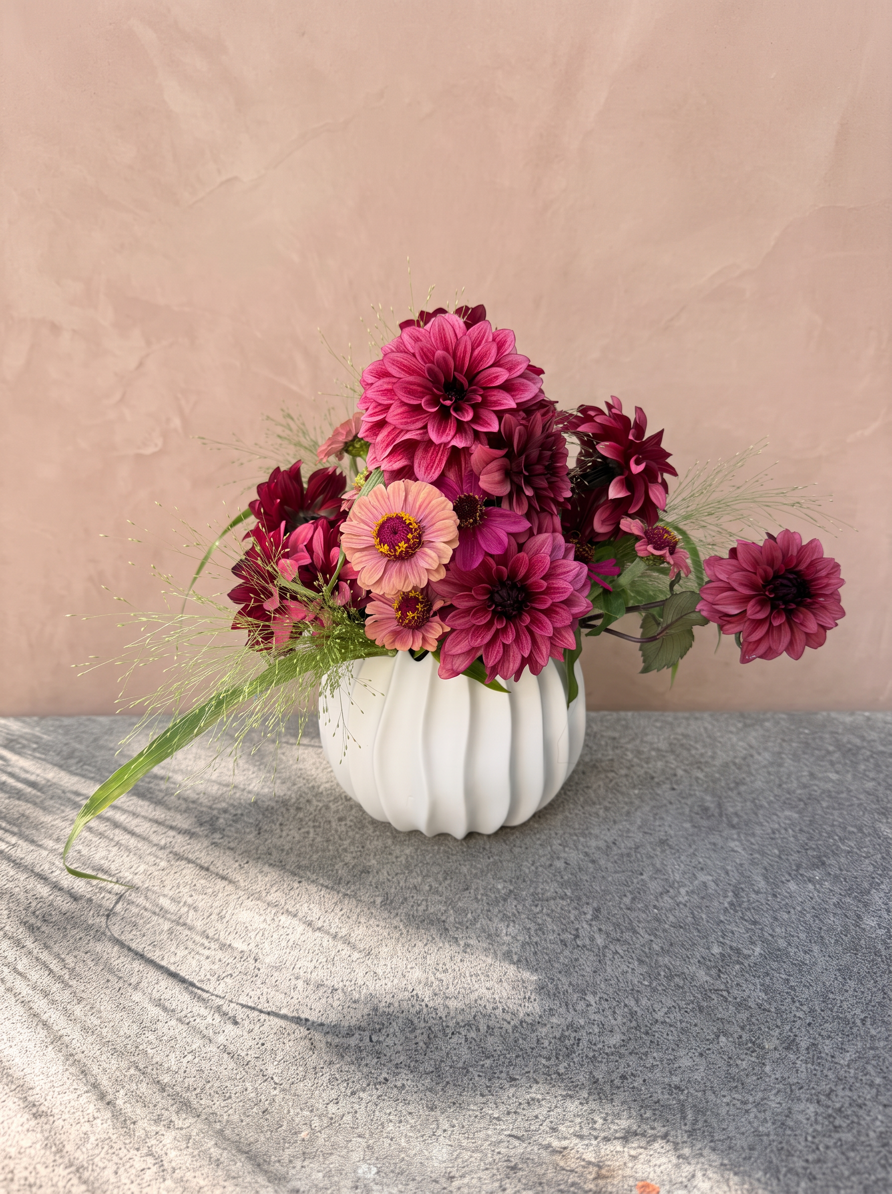 Burgundy and pink dahlias in a white vase against warm blush plaster