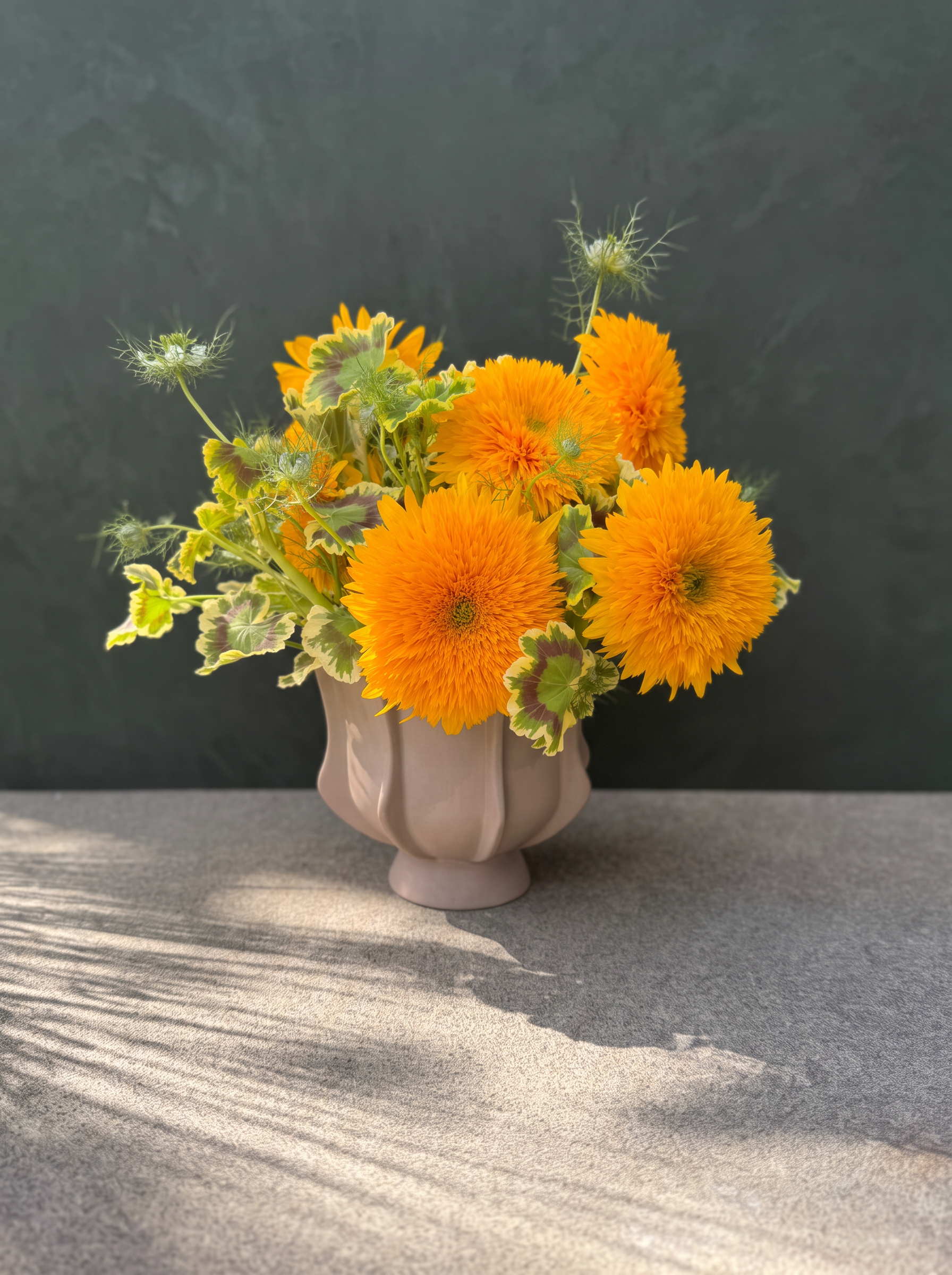 Golden sunflowers in a taupe vase against a charcoal green wall